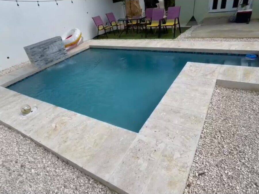 Piscina en forma de L con aceras de travertino recién instaladas