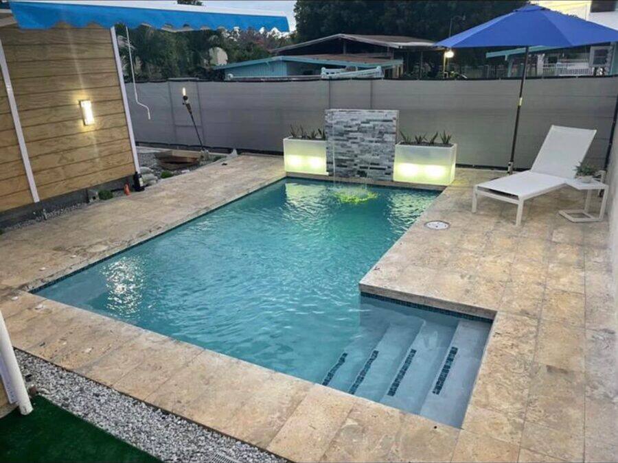Piscina con muro de piedra iluminado y zona de descanso